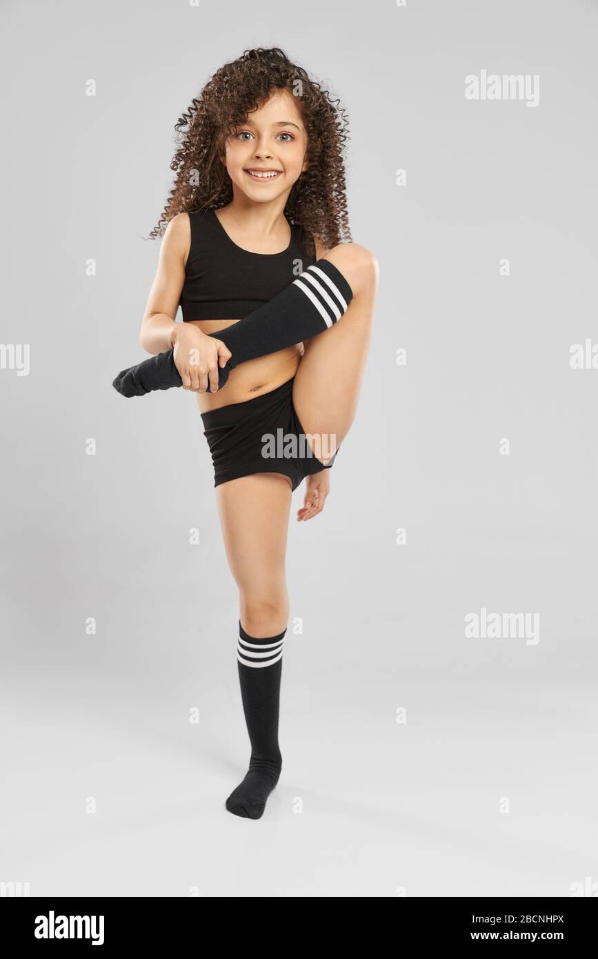 Front view of smiling girl in sportswear and knee socks posing with leg up,  looking at camera, isolated on gray studio background. Little female gymna  Stock Photo - Alamy