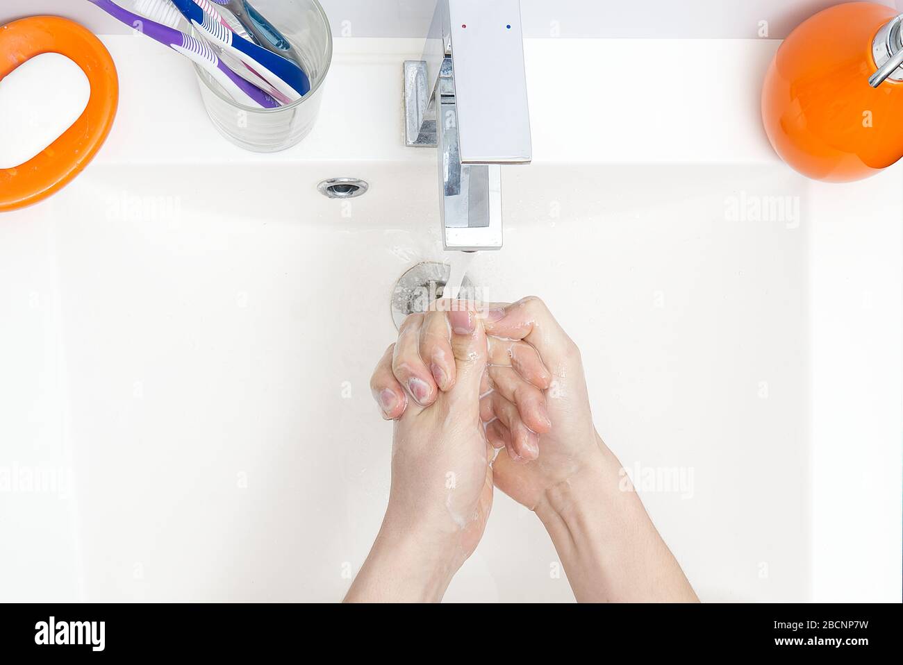 Washing of hands with soap under running water in white sink. close ...
