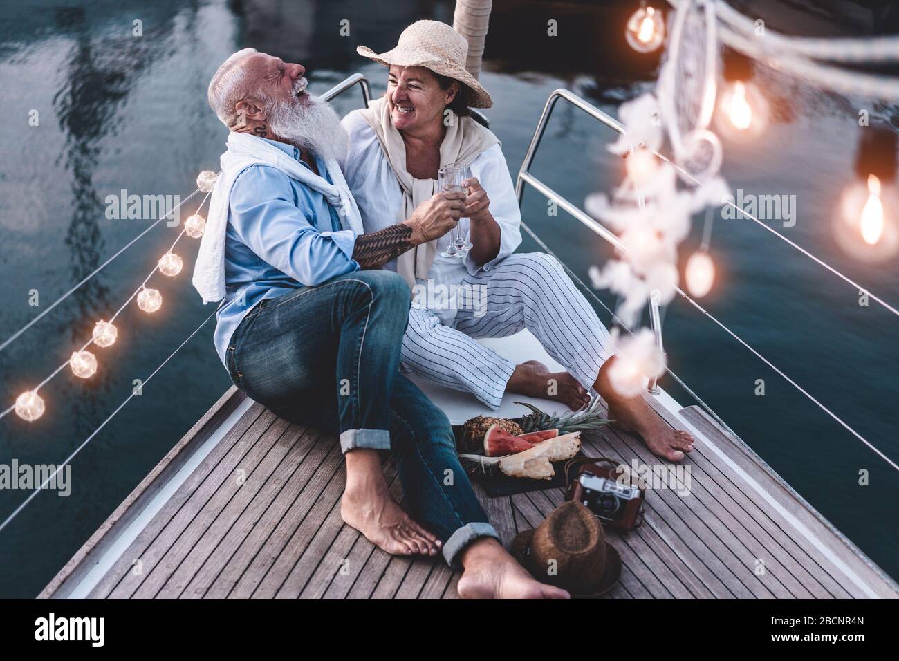Senior couple cheering with champagne on a sailboat during summer vacation - Old people having fun together drinking and laughing - Joyful elderly lif Stock Photo