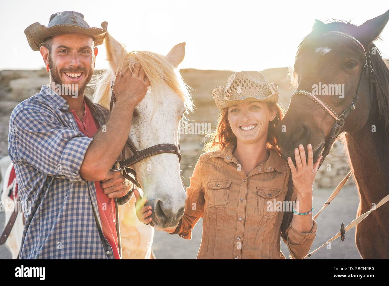 Animals lovers couple taking with bitless horses during sunny day inside ranch corral - Happy people having fun training at their farm - Love and wild Stock Photo