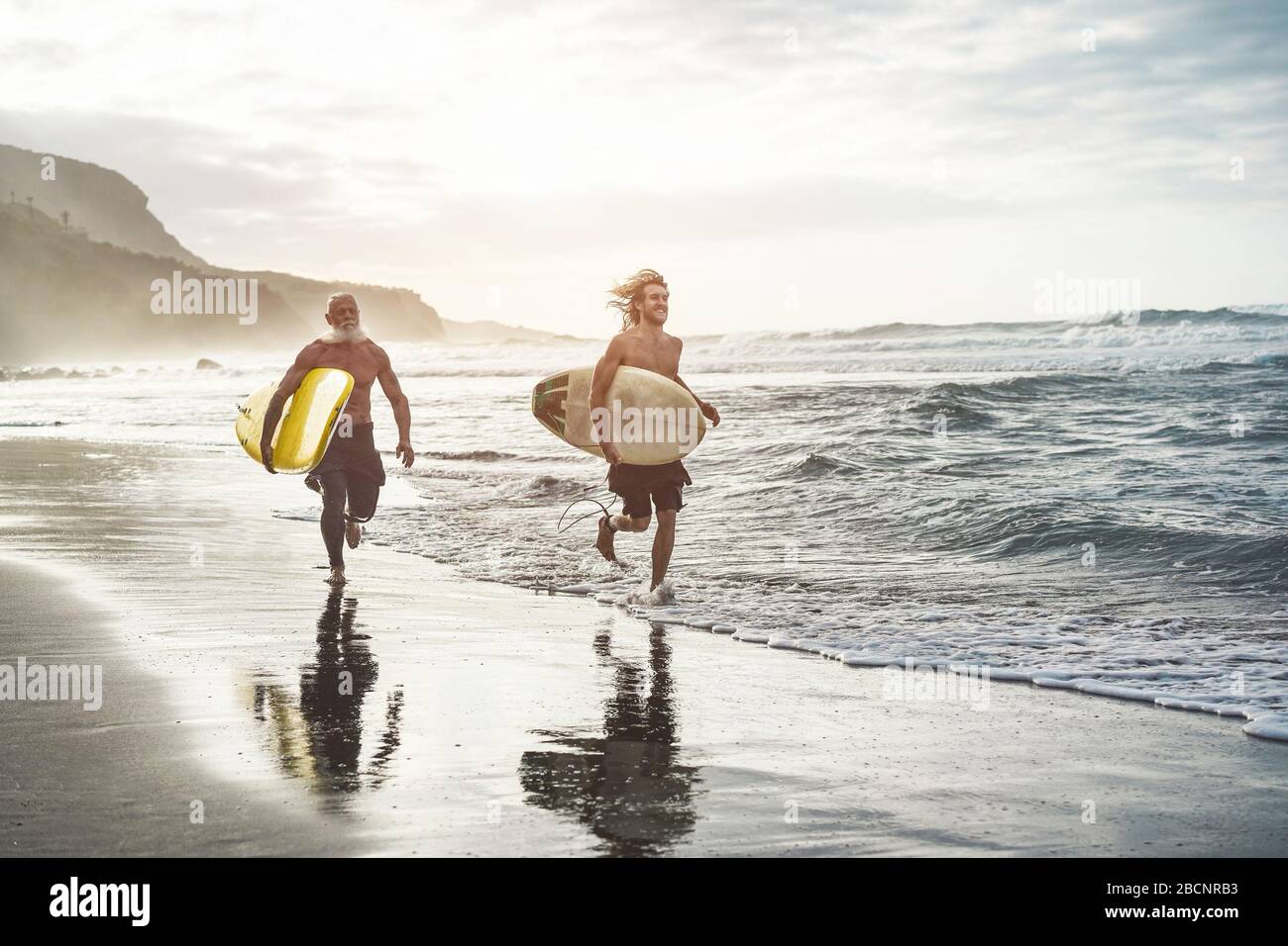 Multigeneration friends going to surf on tropical beach - Family people having fun doing extreme sport - Joyful elderly and healthy lifestyle concept Stock Photo