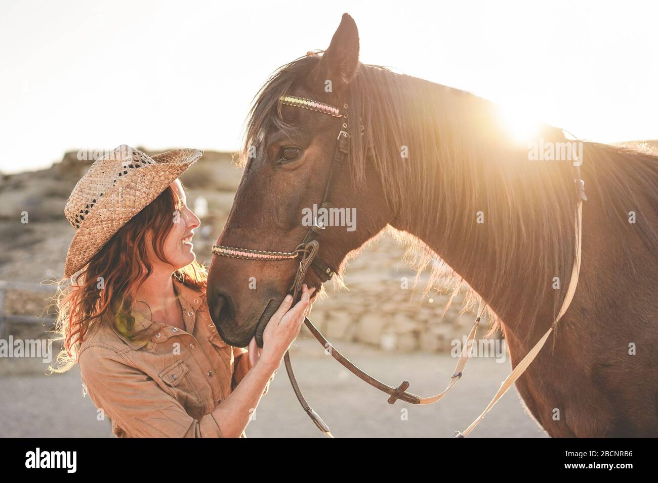Young farmer woman playing with her bitless horse in a sunny day inside corral ranch - Concept about love between people and animals - Focus on girl f Stock Photo