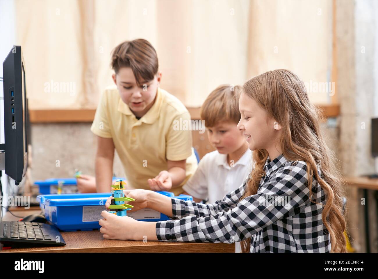 Interesting building kit for kids on table with computers. Side view of boys and girl creating toys. Science engineering. Nice interested friends chat Stock Photo