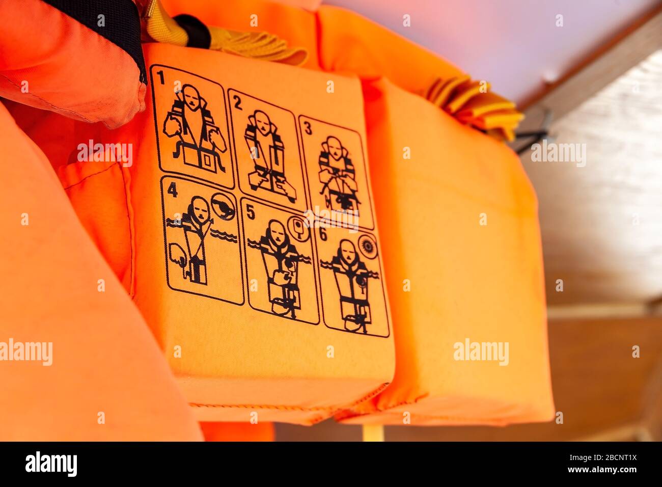 Orange life vests on a ship, closeup on the use instructions, detail How to put on, putting on a life jacket, shallow dof. Personal flotation device Stock Photo
