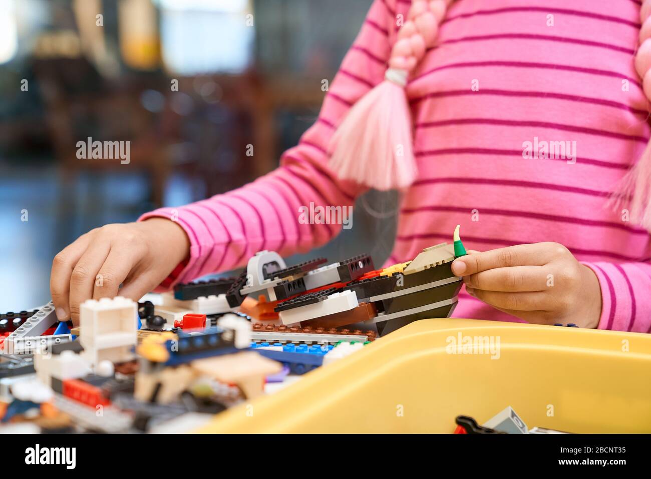 Front view of building kit for kids creating toys, having positive emotions and joy. Crop of incognito african girl working on project, hands taking c Stock Photo