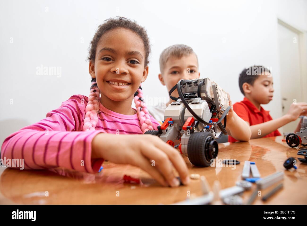 Front view of building kit for group of three multiracial kids creating toys, having positive emotions and joy, african girl smiling and looking at ca Stock Photo