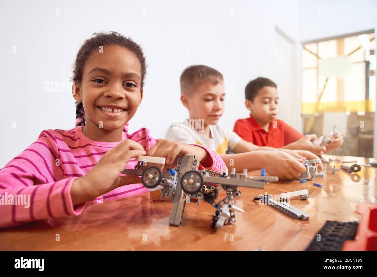 Side view of building kit for group of three multiracial kids creating toys, having positive emotions and joy, african girl smiling and looking at cam Stock Photo