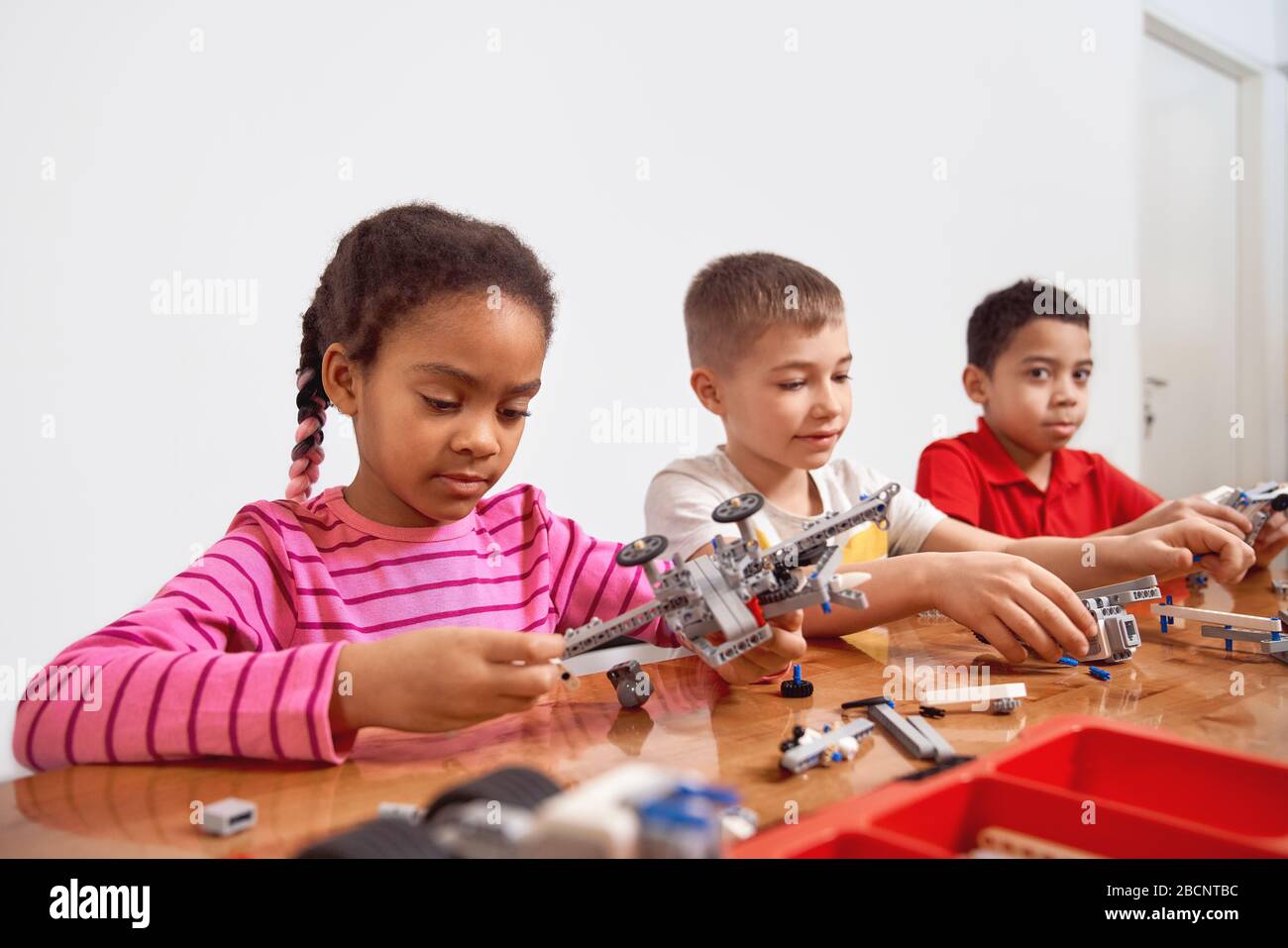 Side view of building kit with colorful peices in box for group of three multiracial kids creating toys, having positive emotions and joy. Close up of Stock Photo
