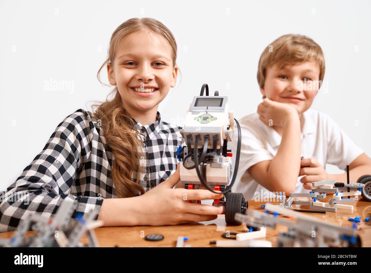 Front view of boy and girl creating robot using building kit for kids on table. Nice interested friends smiling, lookig at camera and working on proje Stock Photo