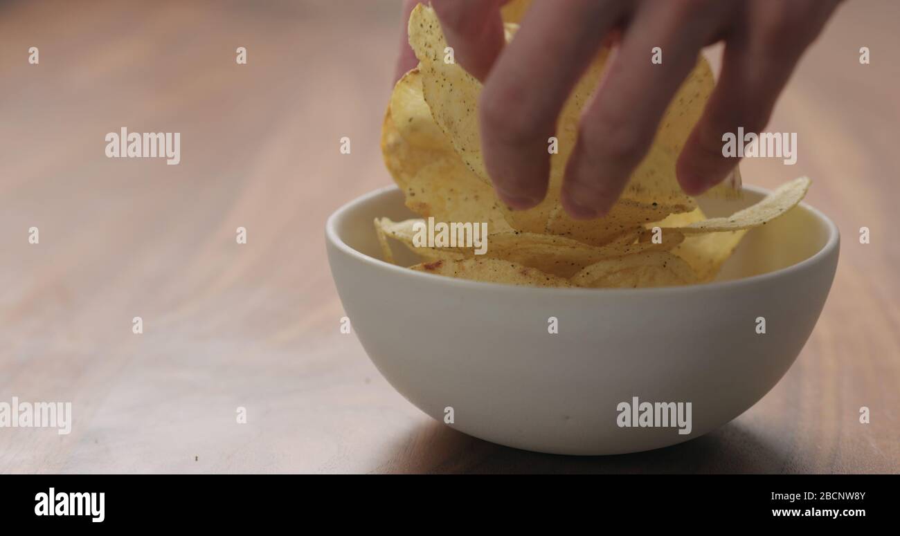 man hand put black pepper seasoned potato chips in white bowl on walnut