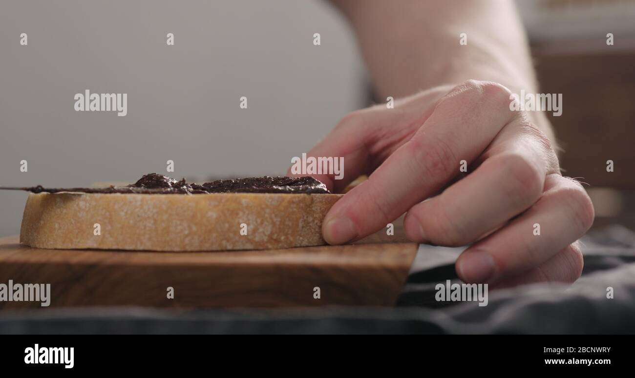 man spreading chocolate nut spread on ciabatta slice on olive board Stock Photo
