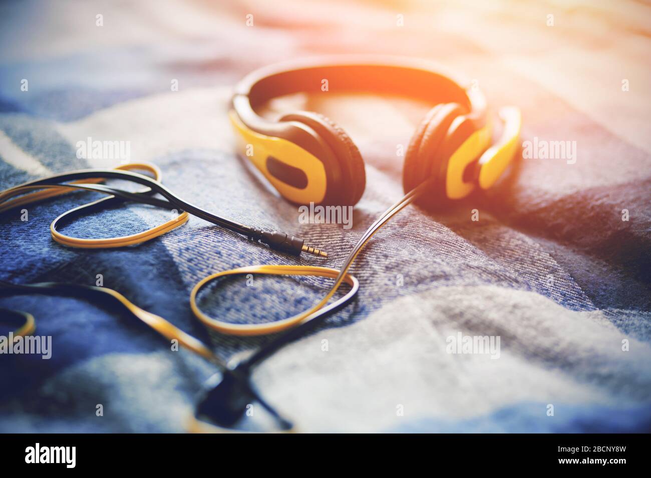 Yellow headphones with a microphone lie on a blue plaid blanket, illuminated by bright sunlight. Music and inspiration. Stock Photo