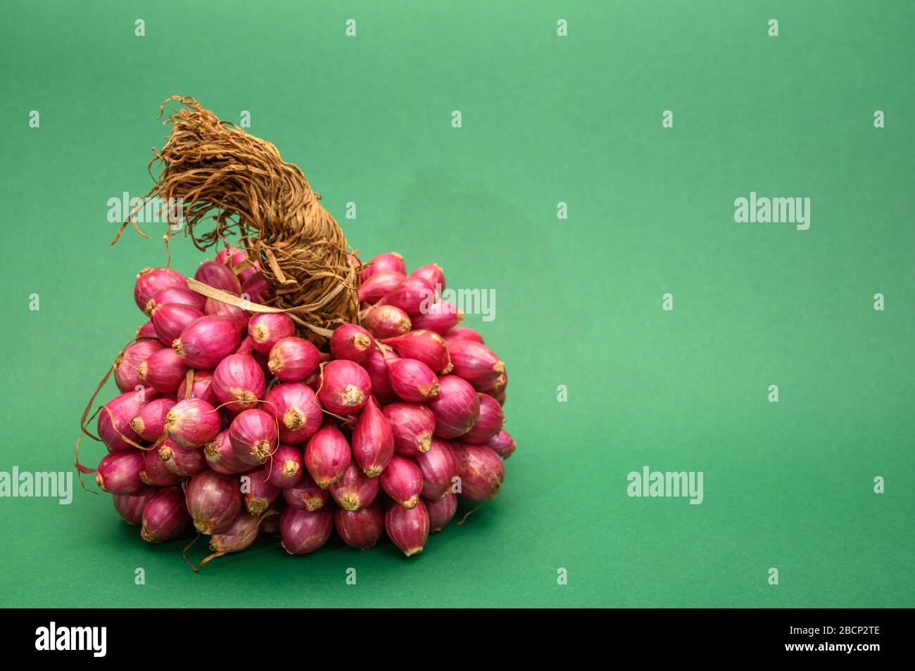 Bunch of high quality small red shallot sambar onions from India on green background Stock Photo