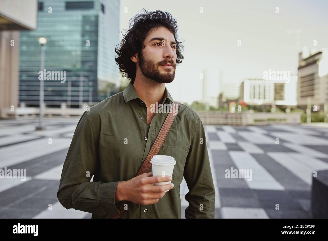 Young businessman holding takeaway coffee cup standing outdoor while looking away and thinking Stock Photo