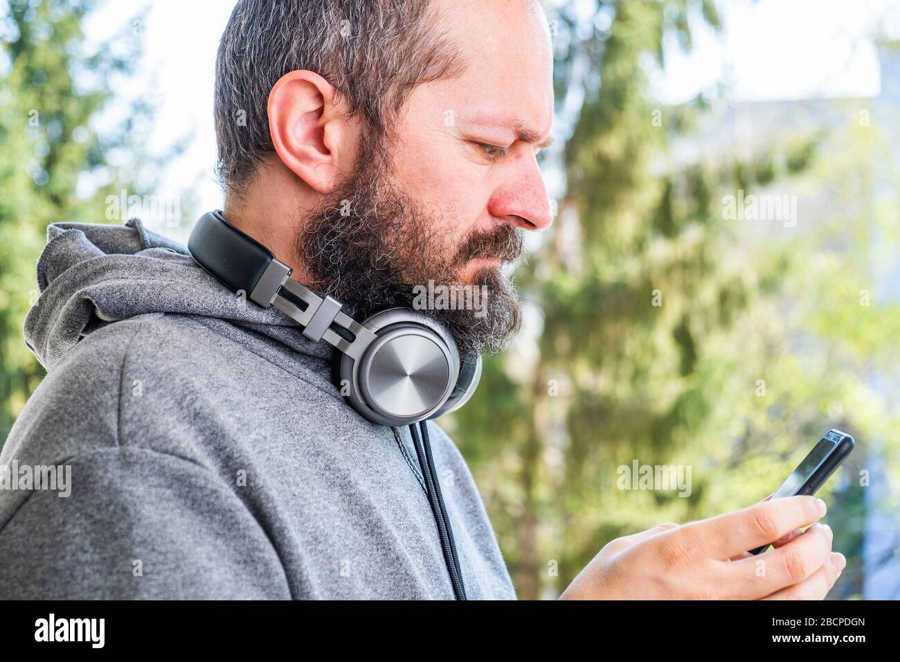 Bearded adult man in hoodie with wireless headphones taking selfie with ...