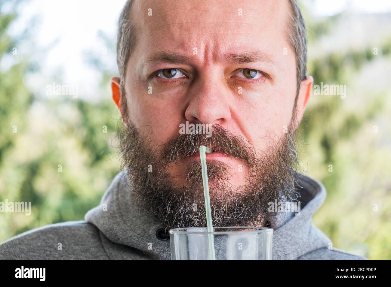 Bearded man in hoodie drinking juice with straw Stock Photo