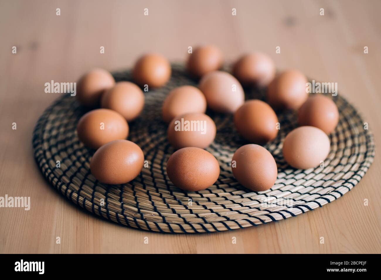 Brown chicken eggs on round wicker kitchen stand on rustic wooden table. Selective focus. Organic food, healthy eating, dieting, protein, farm product Stock Photo