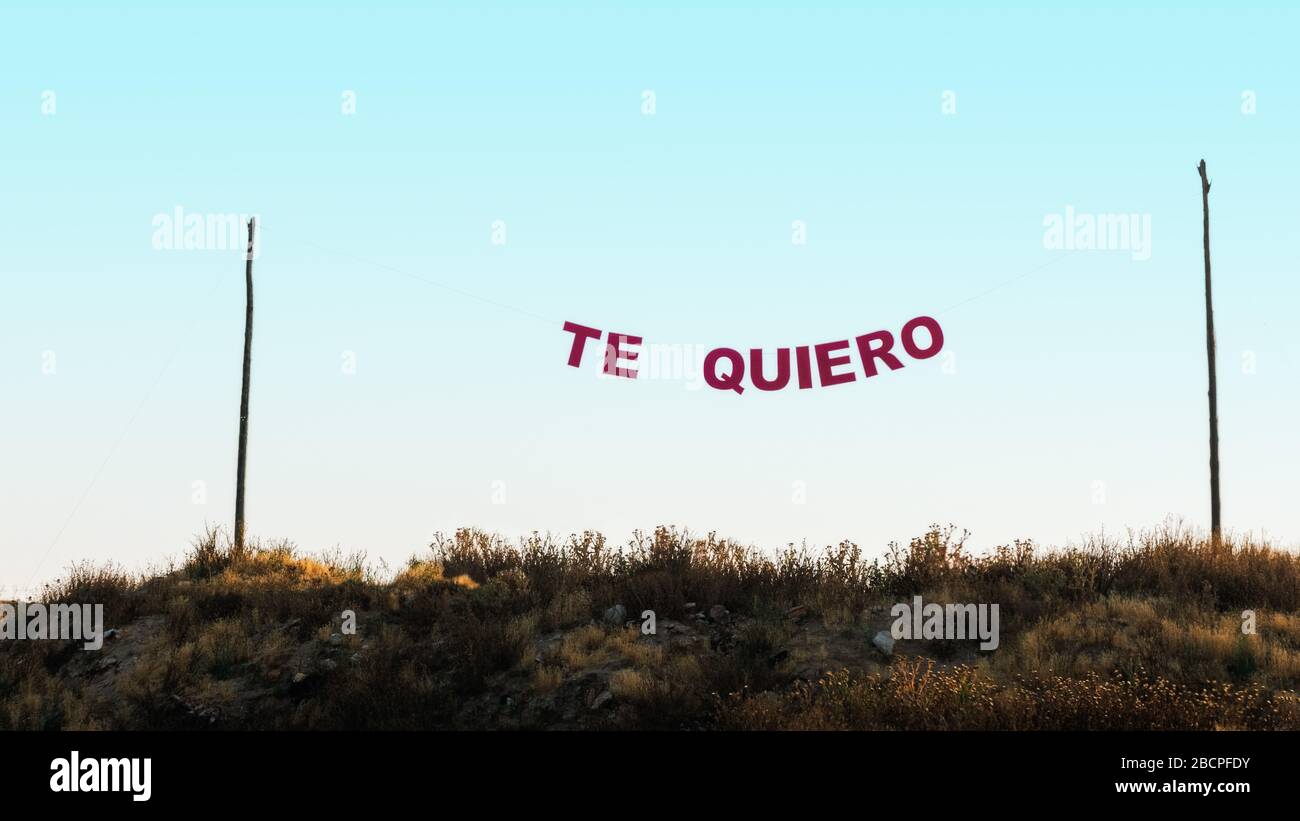 Words 'te quiero' hung between two poles with a rope, in a blue sky. Concept of love. Stock Photo