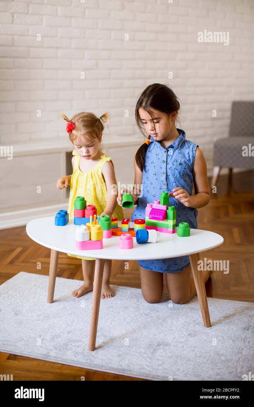 Two cute little girls play with blocks at the table in the room Stock ...