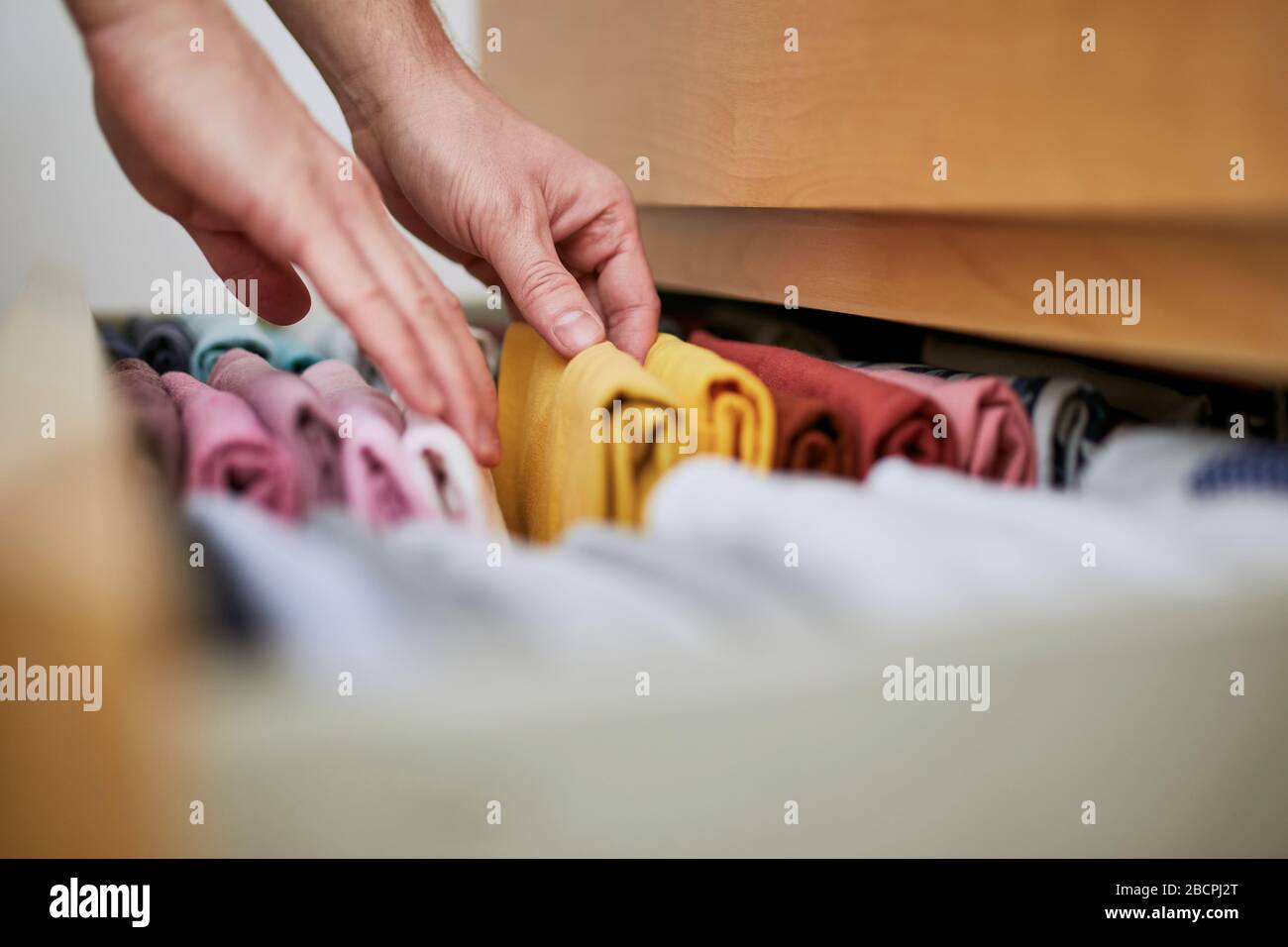 Organizing and cleaning home. Man preparing orderly folded t-shirts in drawer. Stock Photo