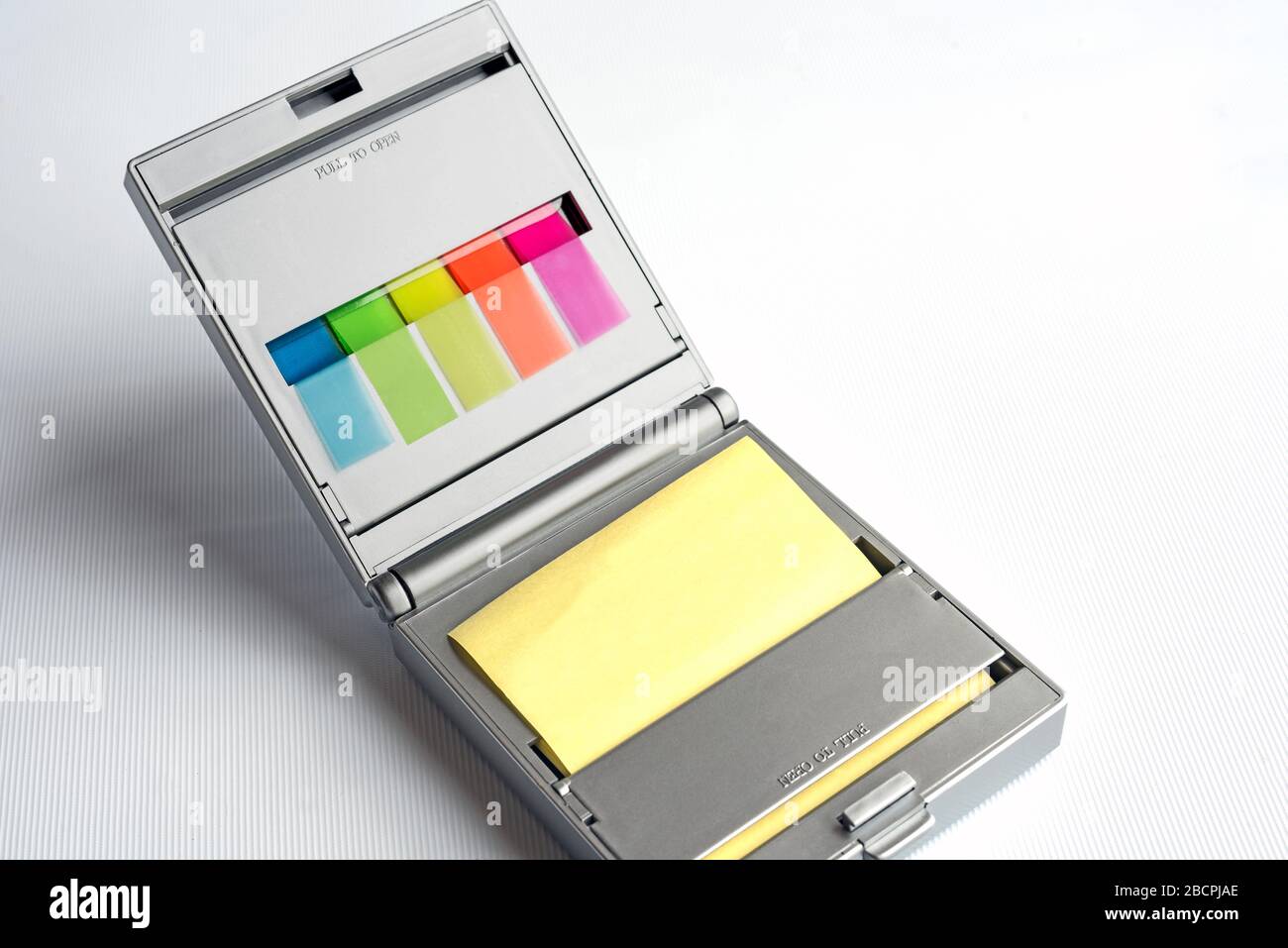 Silver dispenser of yellow postit notes and multi coloured sticky index highlighters against a white background Stock Photo