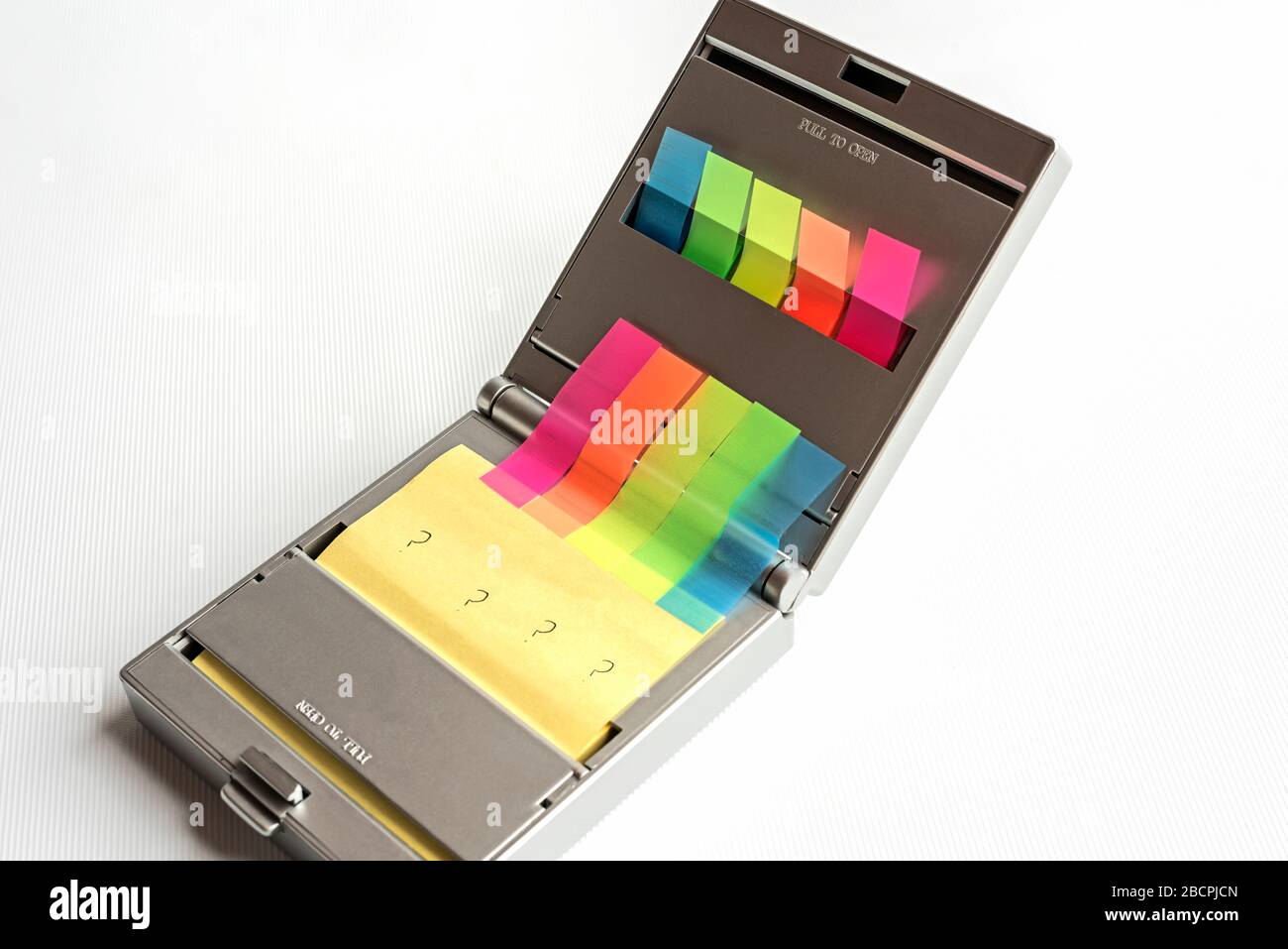 Silver dispenser of yellow postit notes and multi coloured sticky index highlighters against a white background, question marks written on postit note Stock Photo