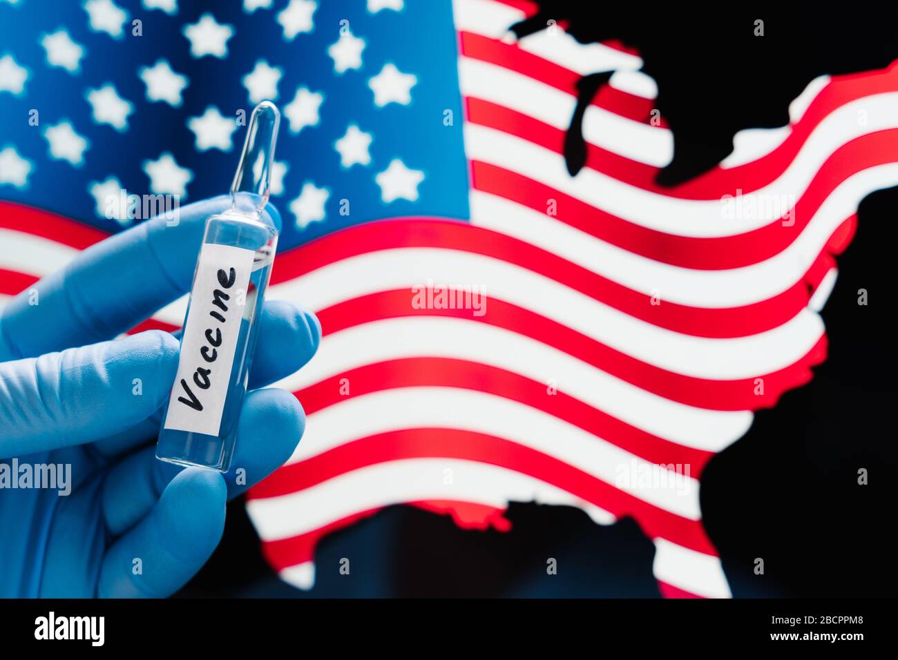 Hand in rubber medical gloves holding vaccine against coronavirus, USA flag in background. Covid-19 in United States of America. Virus outbreak and va Stock Photo