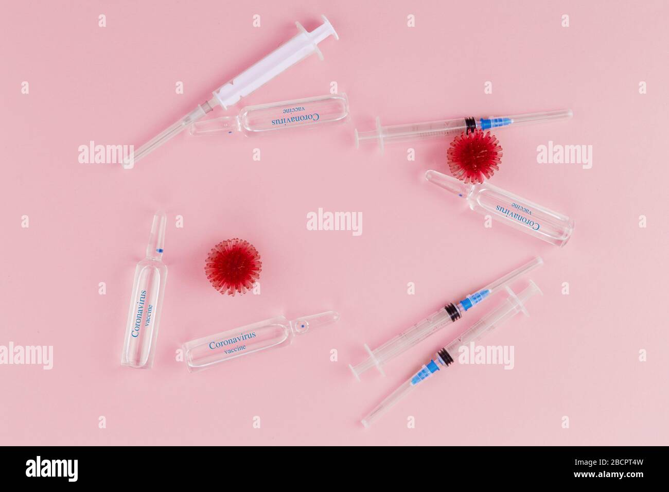 Abstract model of coronavirus infection of the strain Coronavirus. Red virus, syringe and ampoules with medicine on a pink background. On ampoules the blue inscription Coronavirus vaccine. Stock Photo