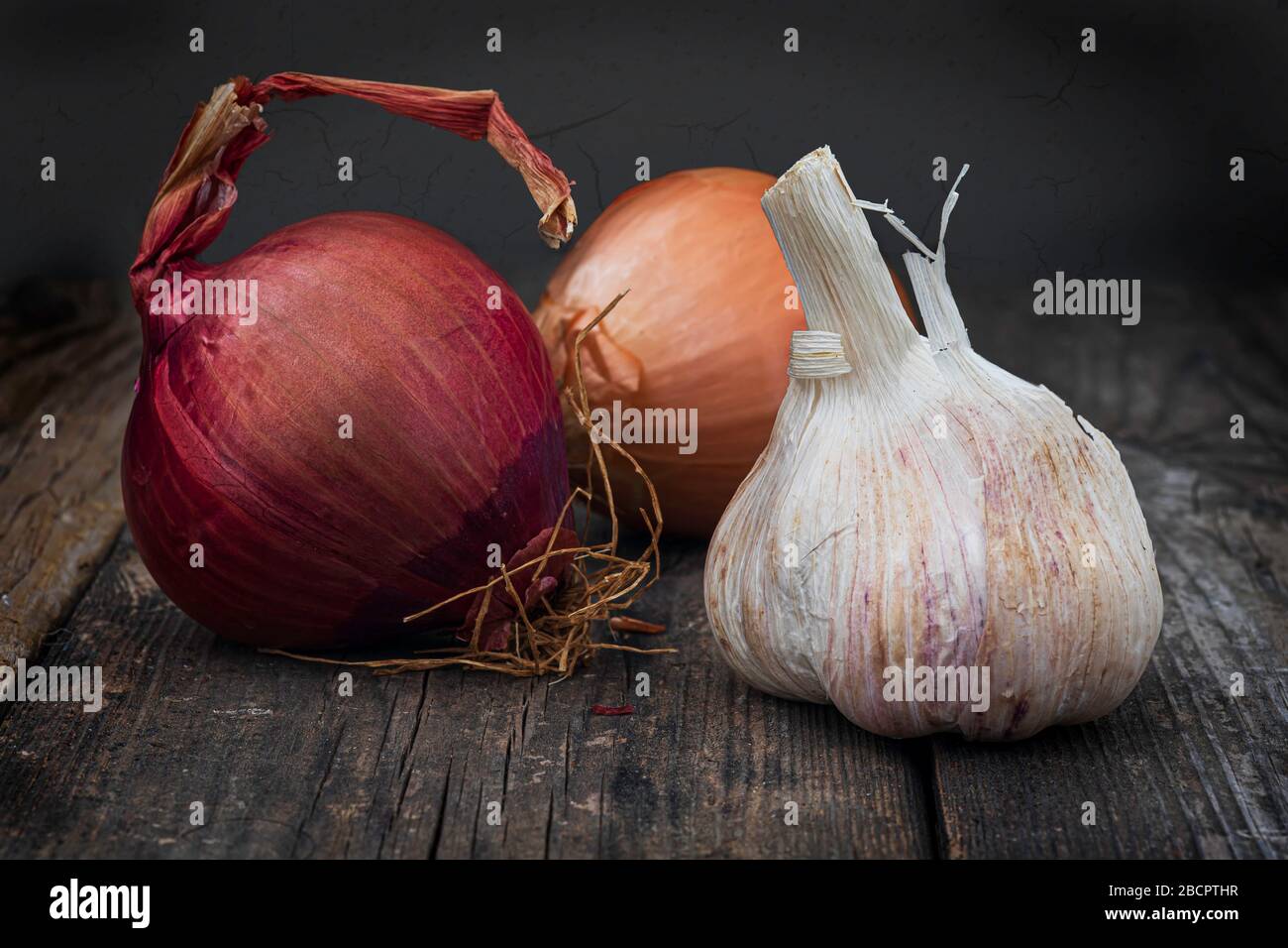Two onions and a head of garlic on a wooden table close up. Food background Stock Photo