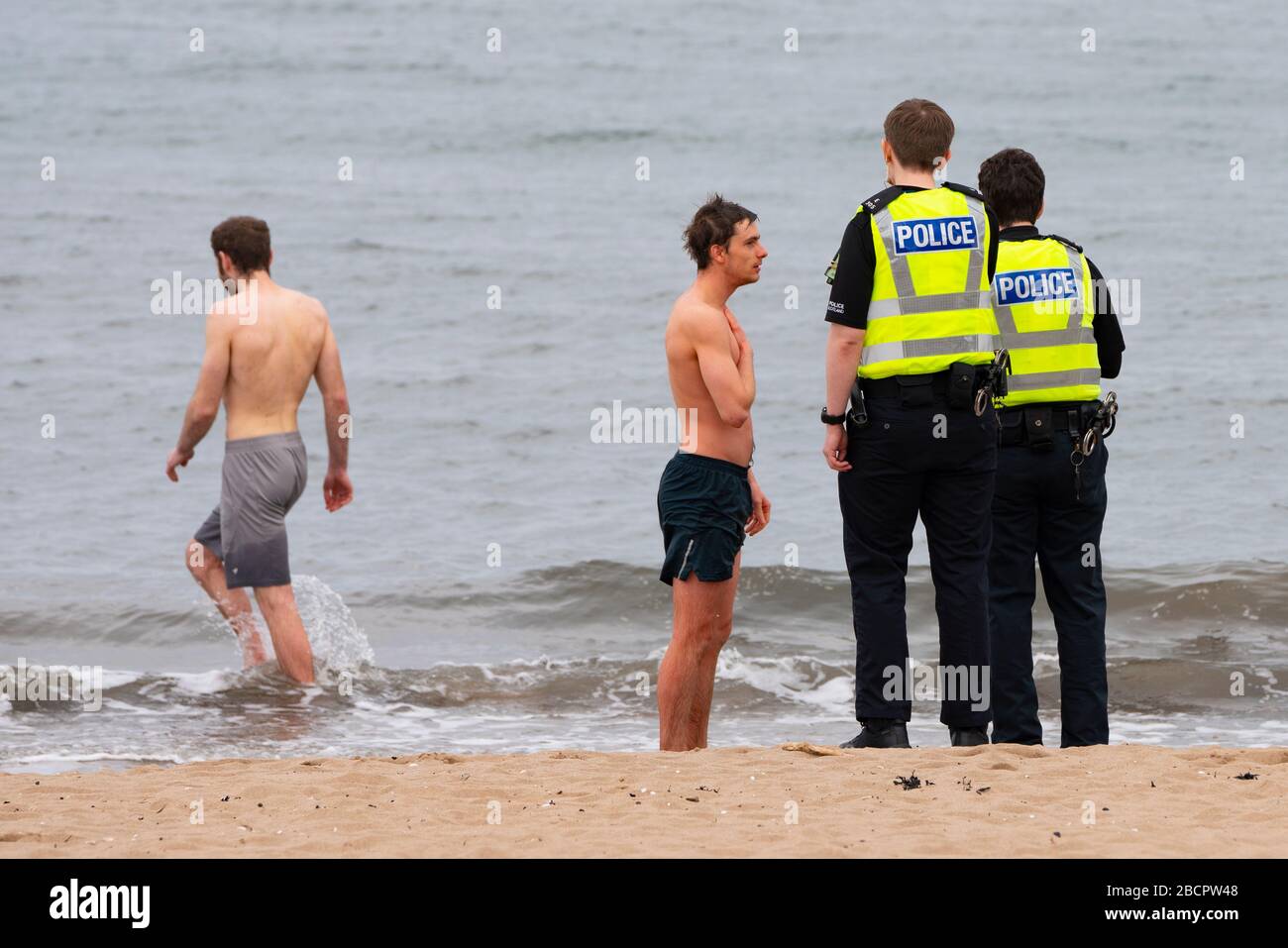 Portobello, Edinburgh, Scotland, UK. 5 April, 2020. On the second Sunday of the coronavirus lockdown in the UK the public are outside taking their daily exercise. Pictured. Police talk to men in swimming trunks on beach at Portobello. After discussion the men were allowed to continue with their swim. Iain Masterton/Alamy Live News Stock Photo
