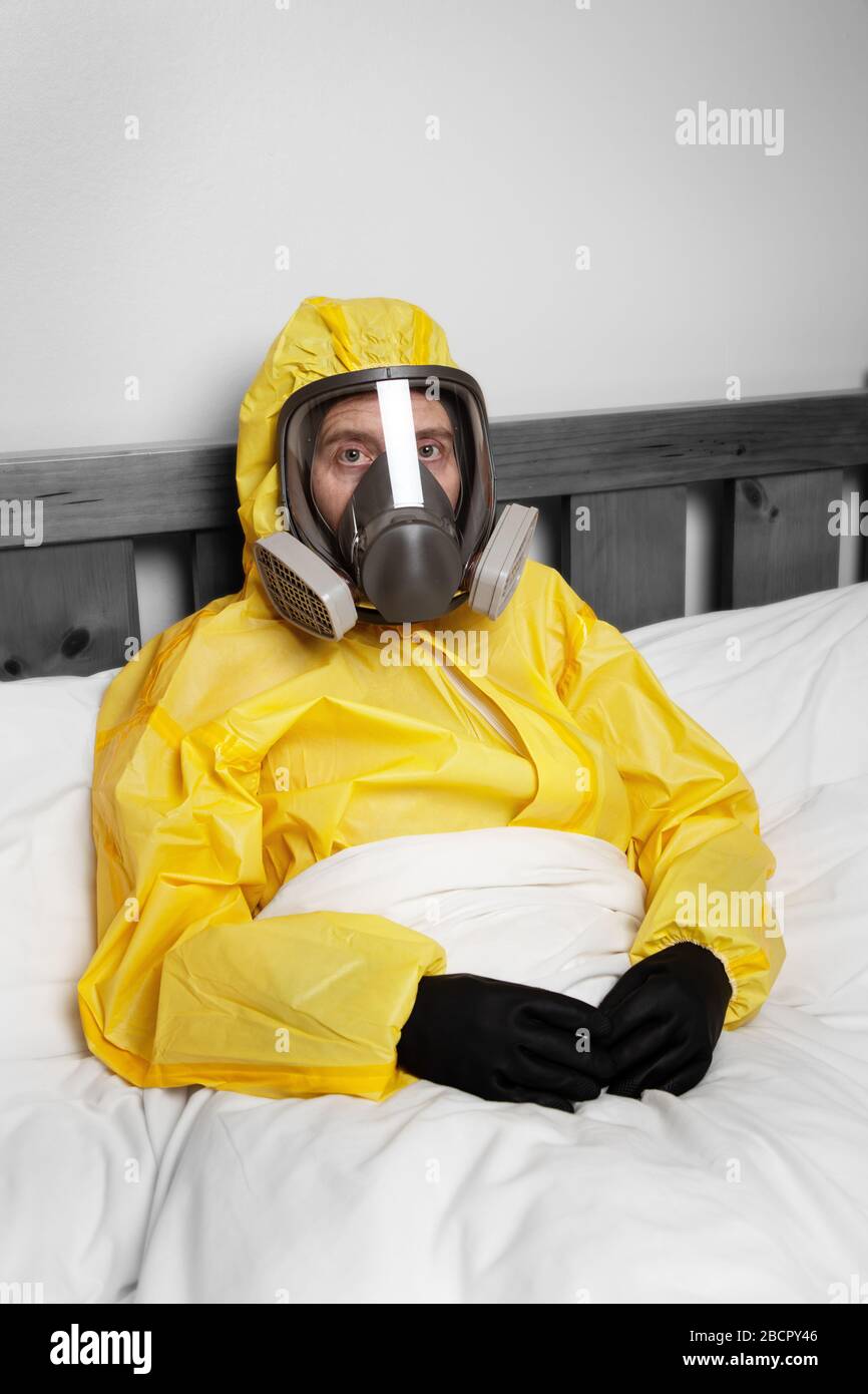 person self isolating in bed wearing a hazmat suit and mask Stock