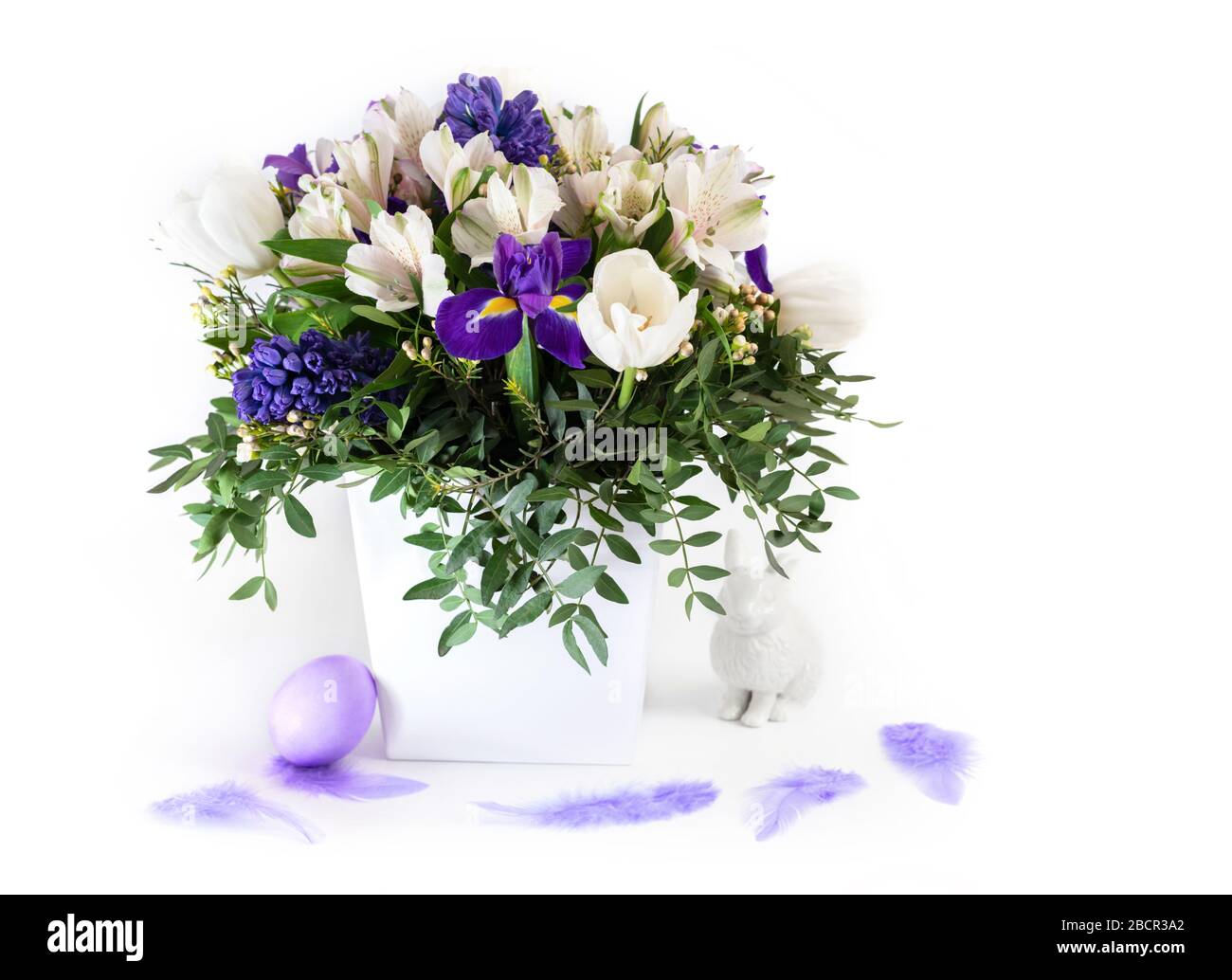 Easter decorations. Spring flowers with an Easter egg and a rabbit on a white background. Copy space. Side view. Stock Photo