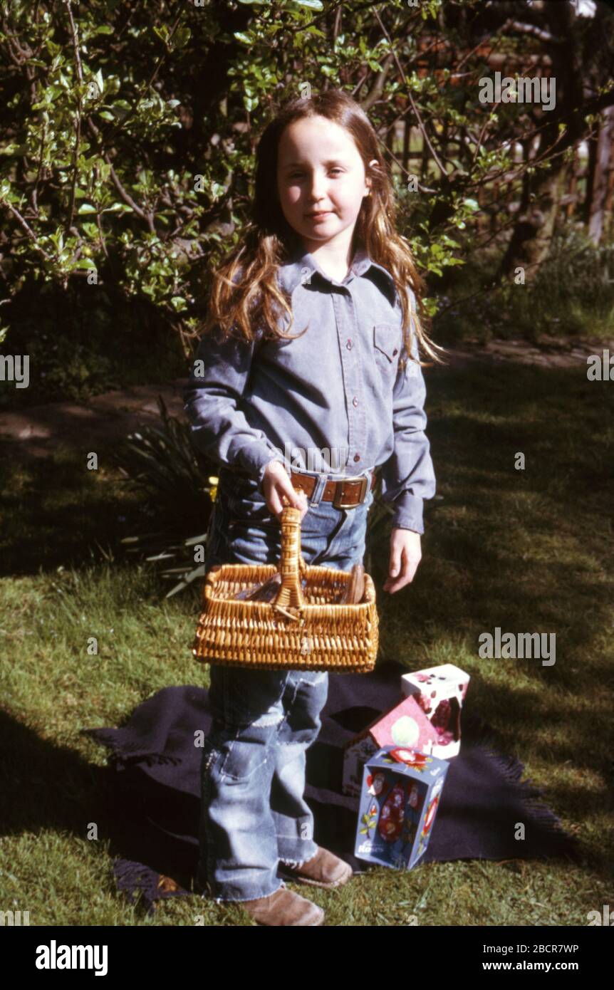 A 9 year old girl with long dark hair wearing blue denim jeans holding her Easter eggs and Lindt Bunny in garden of her family home 1973 UK Stock Photo