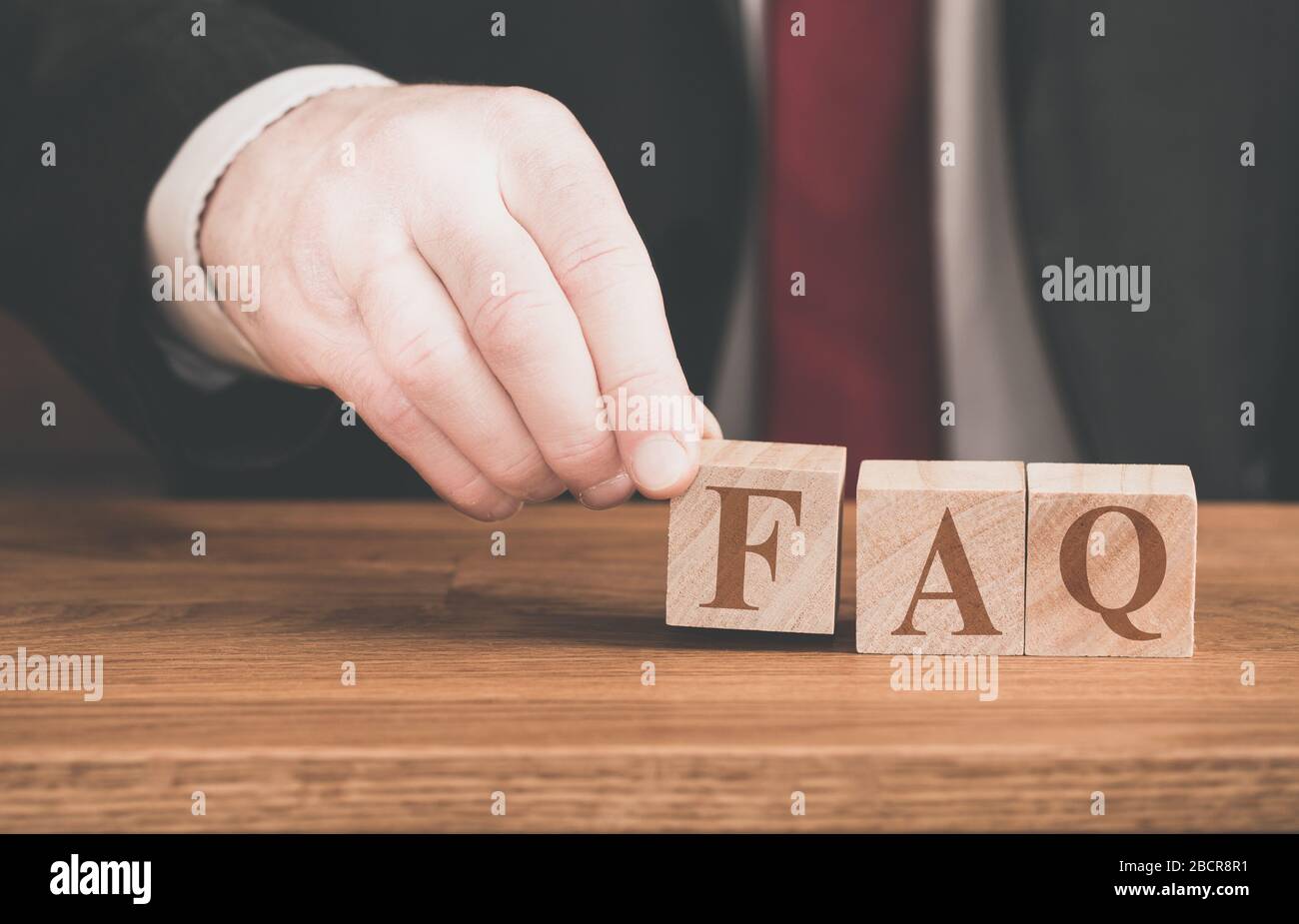 A concept background of a male spelling out the phrase FAQ or frequently asked questions for online website help pages and internet assistance Stock Photo