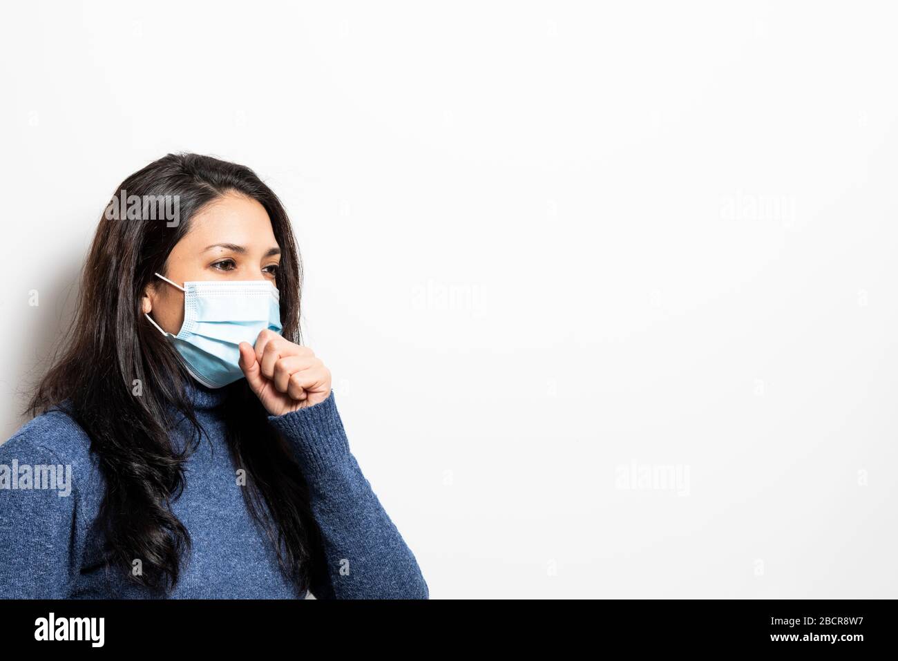 Young woman with mask coughing on a white background. Stock Photo