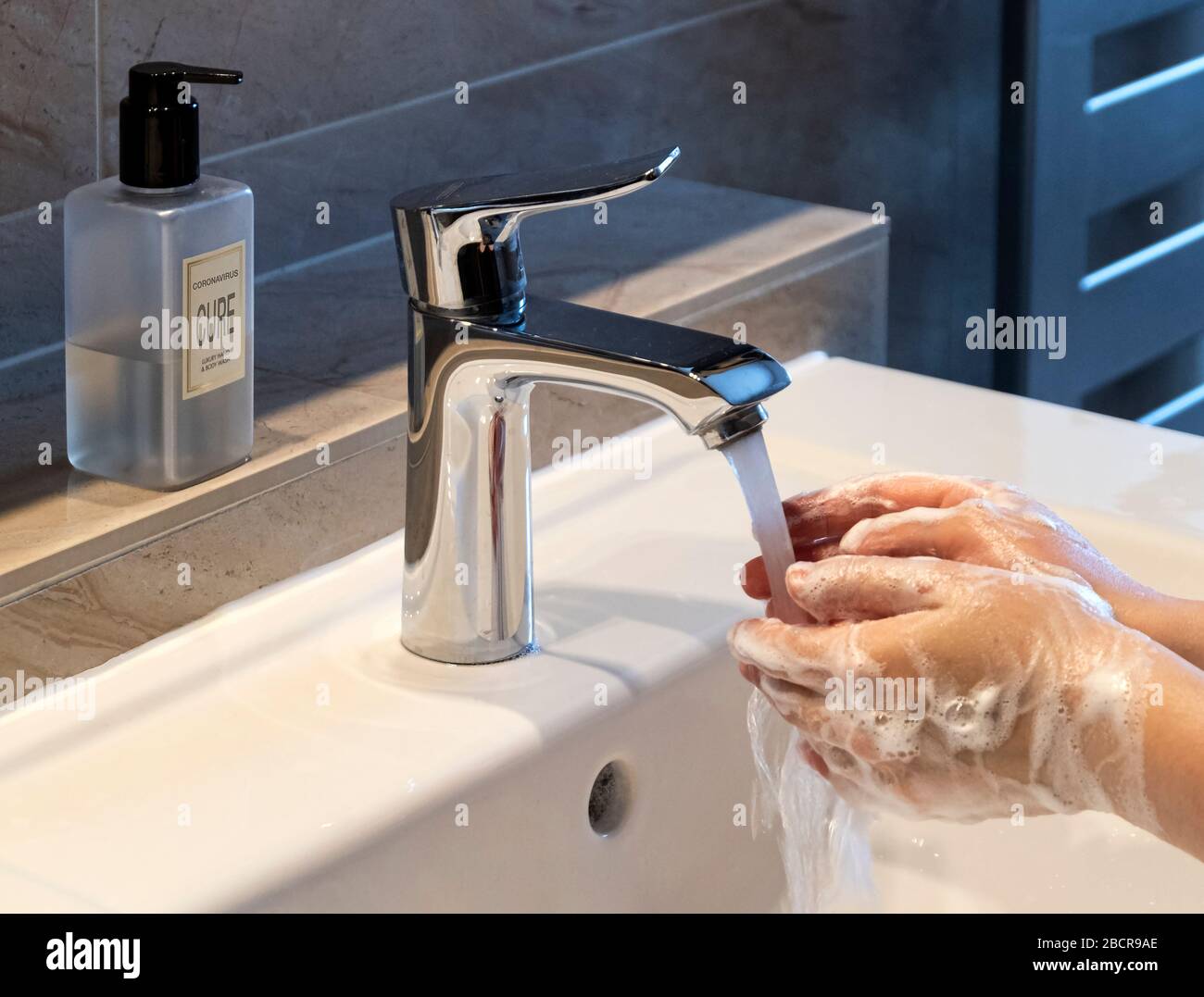 Covid-19 or Coronavirus with Cure written on Soap Dispenser for reduced contamination from washing hands in modern bathroom setting Stock Photo