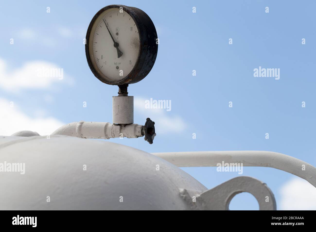 Round industrial pressure gauge mounted on a white gas tank is under blue sky Stock Photo