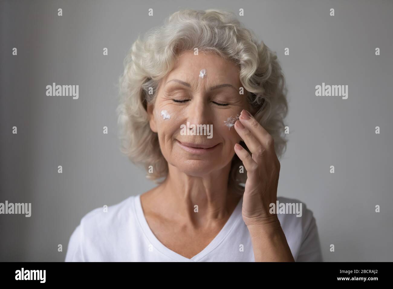 Smiling beautiful middle aged senior retired woman nourishing moisturizing face. Stock Photo