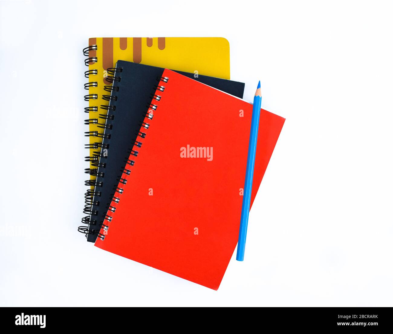 Light blue pencil placed on top of three different colored covered diaries on a white background Stock Photo