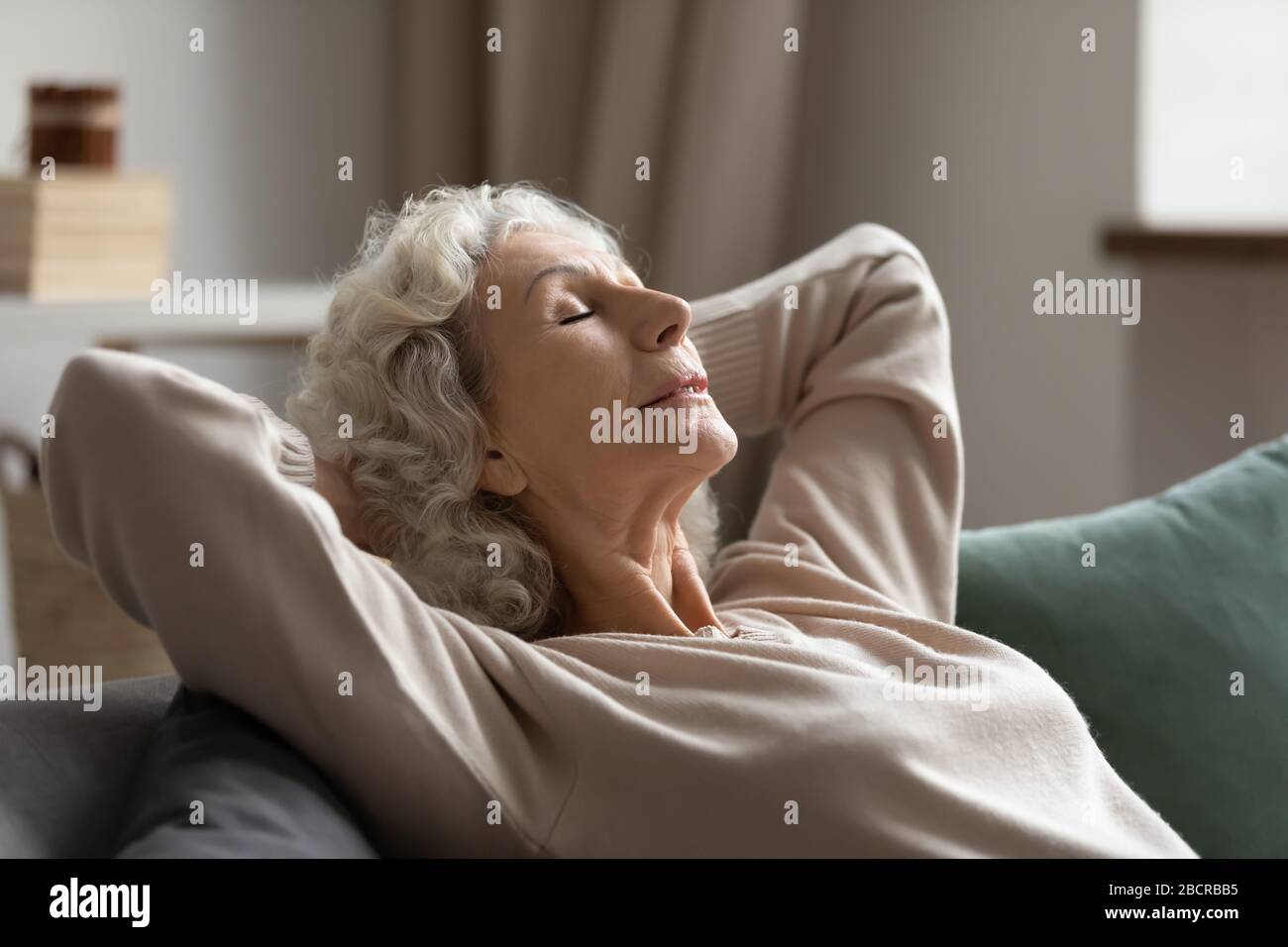 Serene middle aged woman daydreaming on couch. Stock Photo