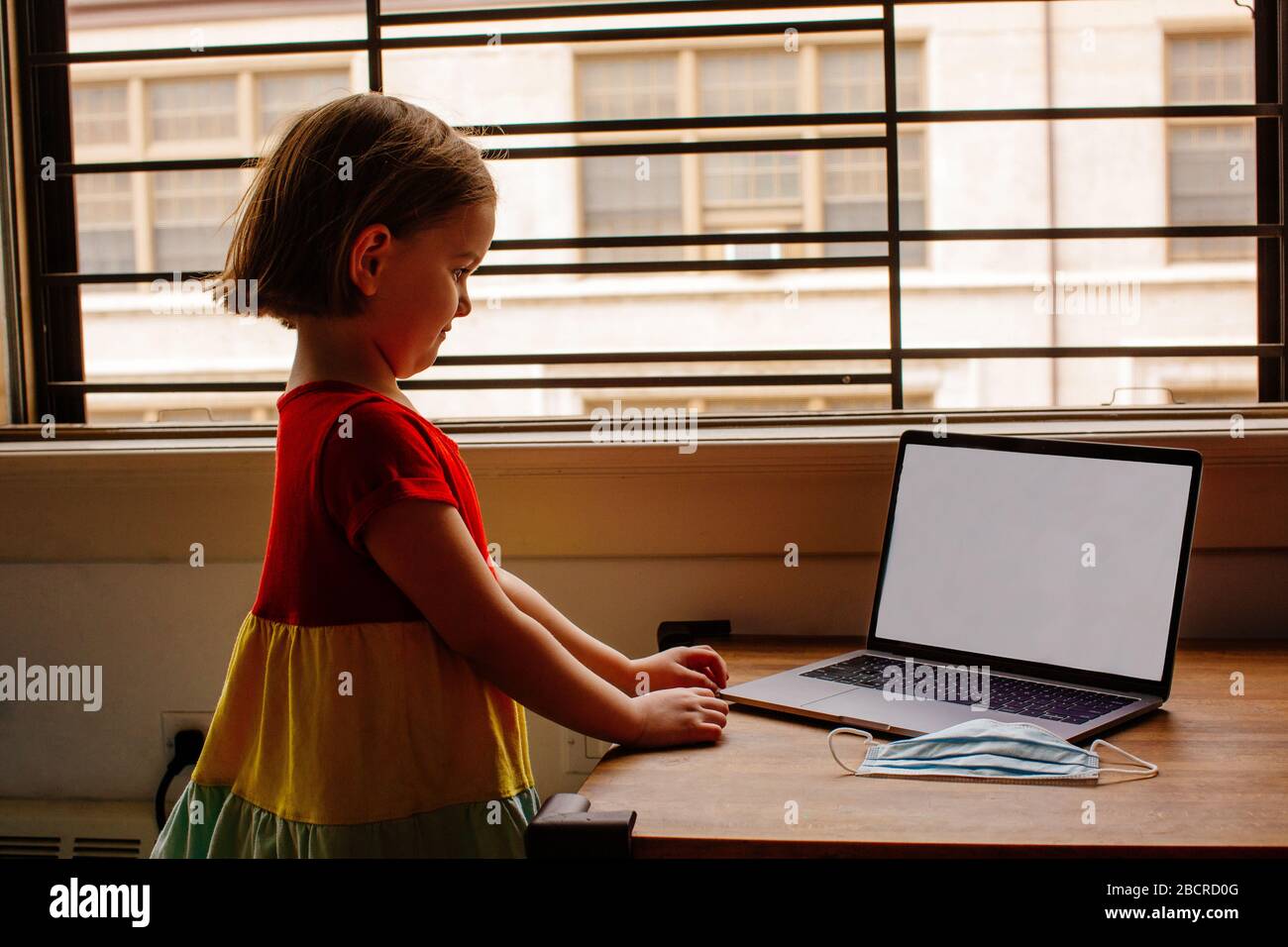 6675Portrait of a small preschool child with laptop computer and surgical face mask, using internet online at home by the window Stock Photo