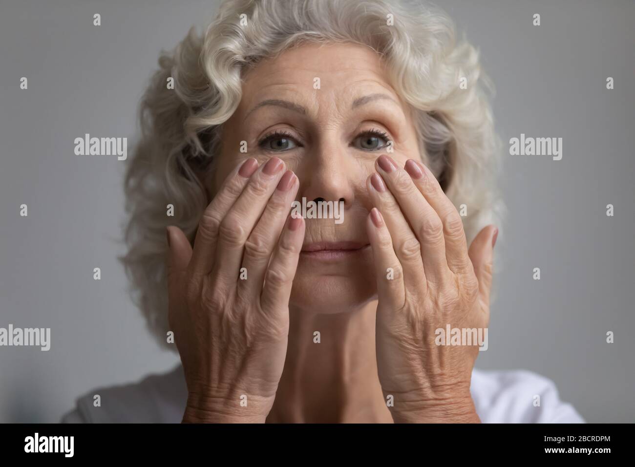 Beautiful elderly retired woman applying nourishing anti age cream. Stock Photo