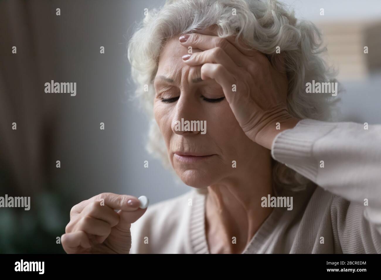 Worrying middle aged grandmother taking pills painkiller. Stock Photo