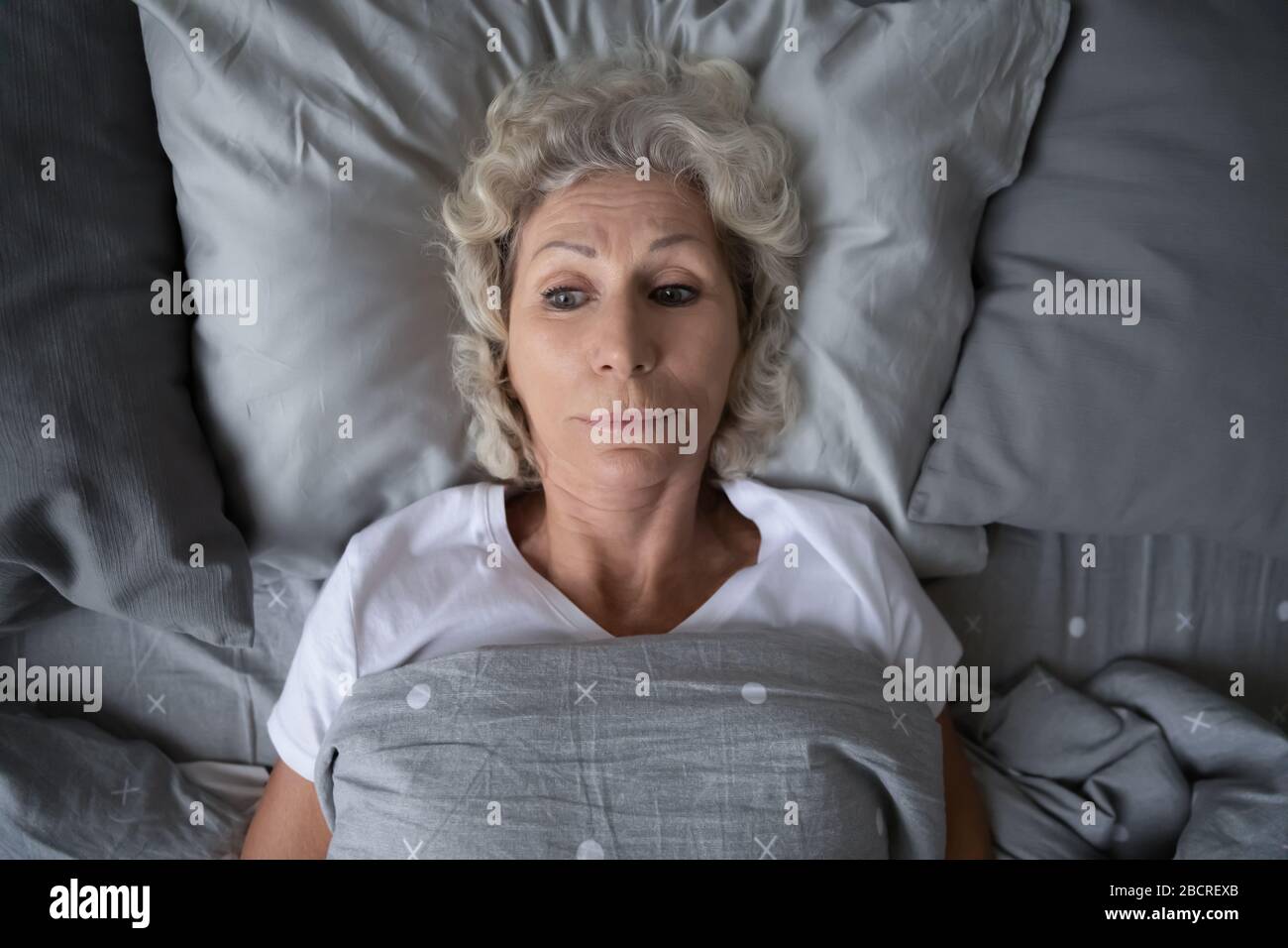 Unhappy mature old grandmother suffering from insomnia at night. Stock Photo