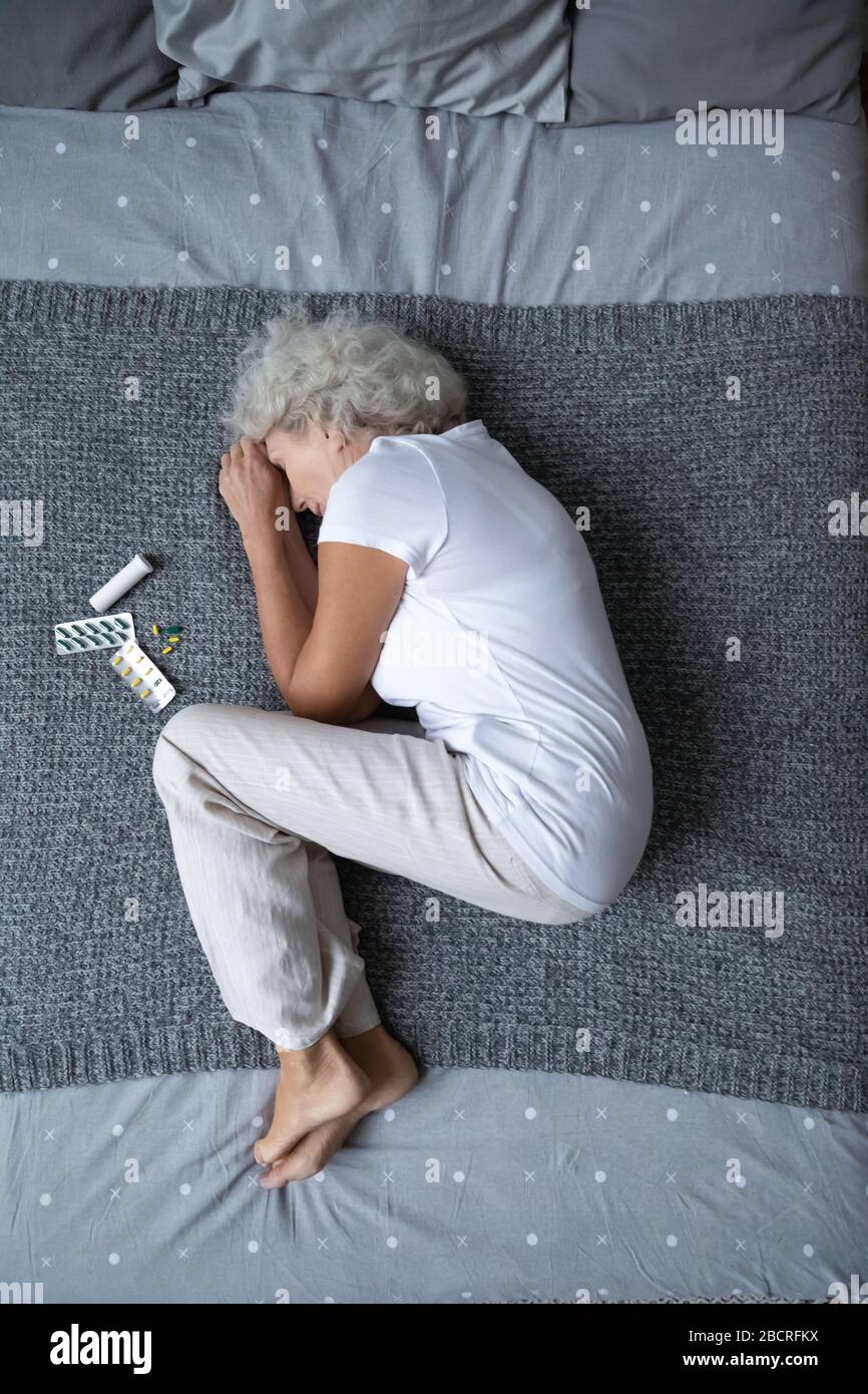 Stressed mature retired woman lying on bed in fetal position. Stock Photo