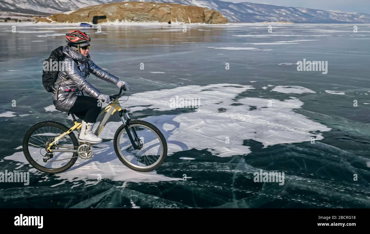 Woman is riding bicycle on the ice. Tires on bike are covered wi Stock