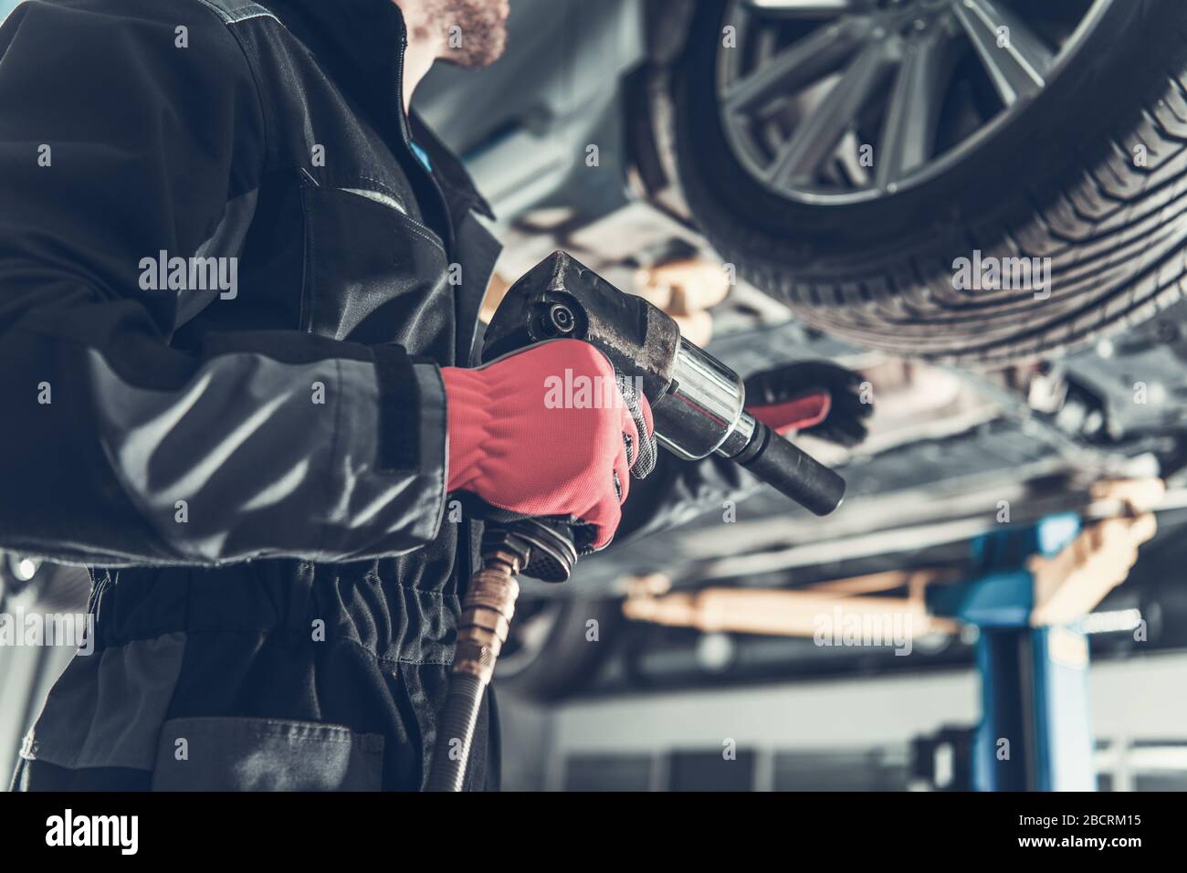 Seasonal Car Tire Replacement. Car Mechanic with Pneumatic Gun In Hand