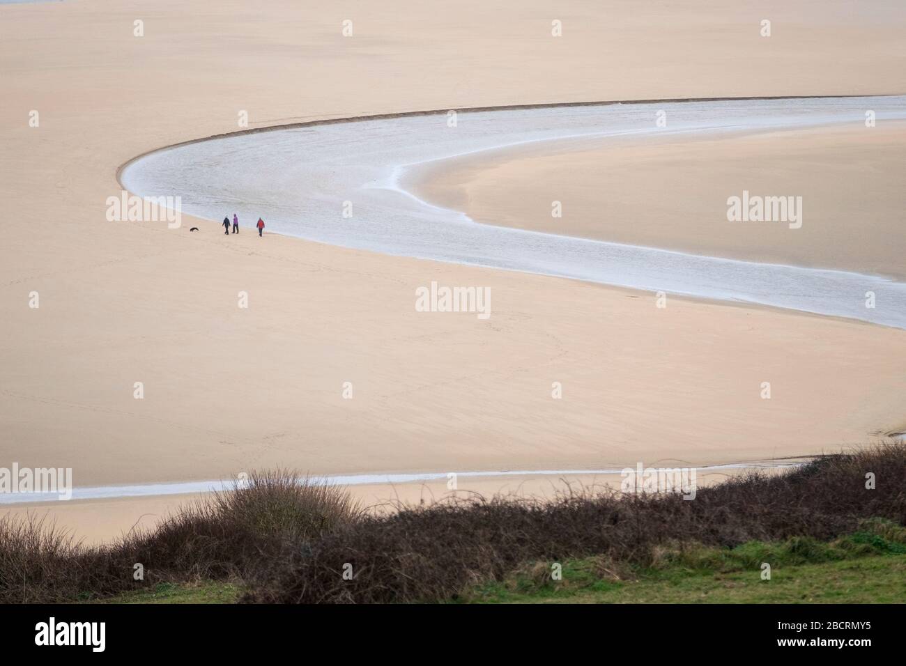 A family with their dog social distancing wher the river Gannel flows in to the sea at Crantock beach, near Newquay, Cornwall Stock Photo