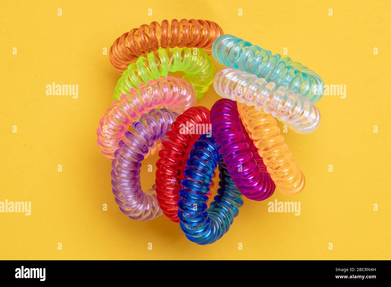 Close-up of multicolored elastic spiral scrunchies or hair bands for women hairstyling over yellow background. Hair care tools from hairdresser and be Stock Photo