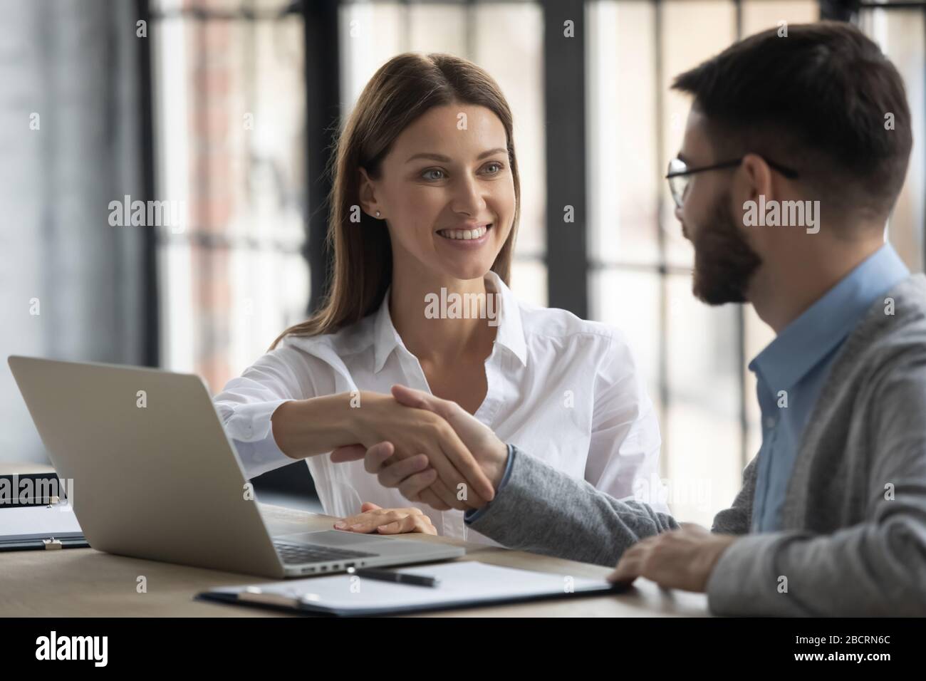 Happy businesswoman shaking hands with man job seeker near laptop. Stock Photo